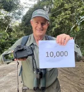 Peter Kaestner holding a 10,000 bird sign with an image of the last species - an orange-tufted spiderhunter